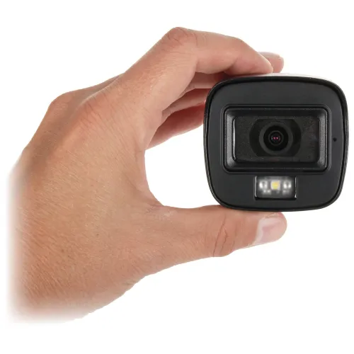 Zdjęcie przedstawia rękę trzymającą małą kamerę z widocznym obiektywem i trzema diodami LED poniżej. Kamera ma kompaktowy, prostokątny kształt i czarną obudowę.