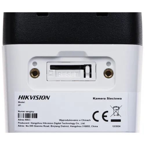 Zbliżenie na tylną część kamery sieciowej Hikvision z widocznym przyciskiem reset i informacjami technicznymi. Na etykiecie znajdują się dane producenta, numer seryjny oraz oznaczenia certyfikacyjne.