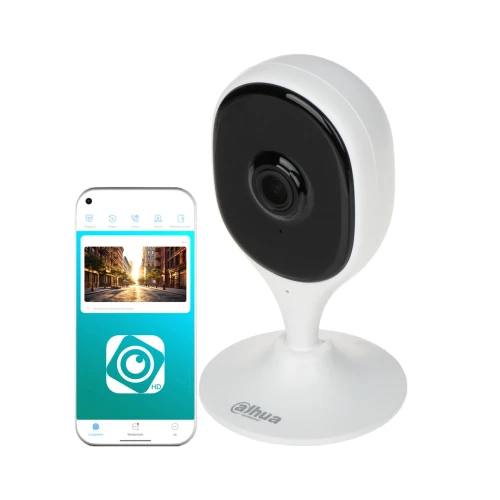 Na zdjęciu znajduje się biała kamera IP o nowoczesnym designie, umieszczona na stojaku. Obok kamery widoczny jest smartfon z aplikacją do monitoringu, pokazującą obraz z kamery.