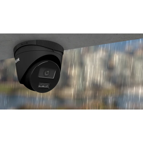 Czarna kamera IP zamontowana jest na suficie, z widocznym obiektywem i diodami LED. W tle znajduje się rozmyty widok miasta.