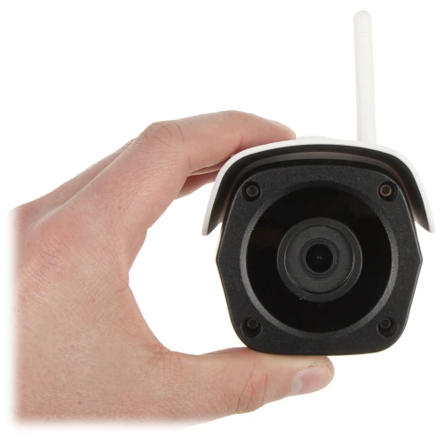 Mała kamera monitorująca z anteną bezprzewodową trzymana w dłoni, ukazująca jej kompaktowy rozmiar. Kamera ma czarny obiektyw i białą obudowę.