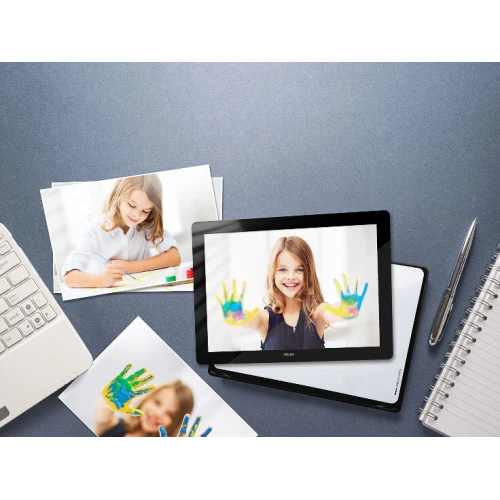 Na zdjęciu znajduje się sterownik gestów Fibaro Swipe w formie eleganckiej, czarnej ramki cyfrowej. Urządzenie jest umieszczone na biurku obok zdjęć, klawiatury i notesu, co sugeruje jego zastosowanie w domowym lub biurowym środowisku.