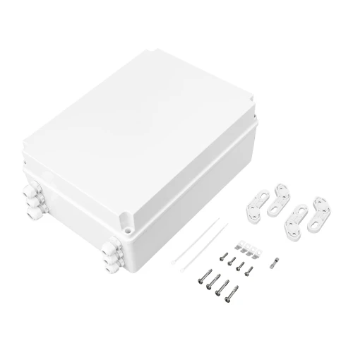 Na zdjęciu znajduje się biały switch PoE BCS UPS IP4 w prostokątnej obudowie z tworzywa sztucznego, wyposażony w kilka złącz kablowych. Obok urządzenia leżą akcesoria montażowe, takie jak śruby, kołki i uchwyty.