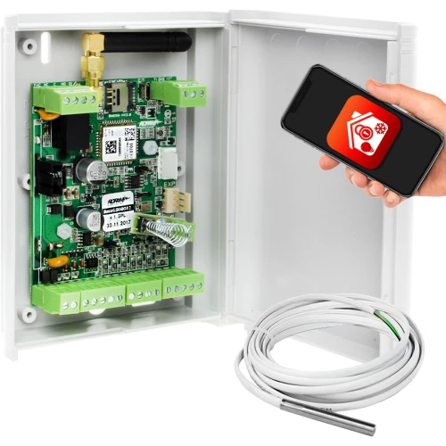 Na zdjęciu znajduje się system monitorowania temperatury zamknięty w białej obudowie z widocznymi elementami elektronicznymi i złączami. Obok znajduje się ręka trzymająca smartfon z aplikacją do zdalnego monitorowania oraz przewód z czujnikiem temperatury.