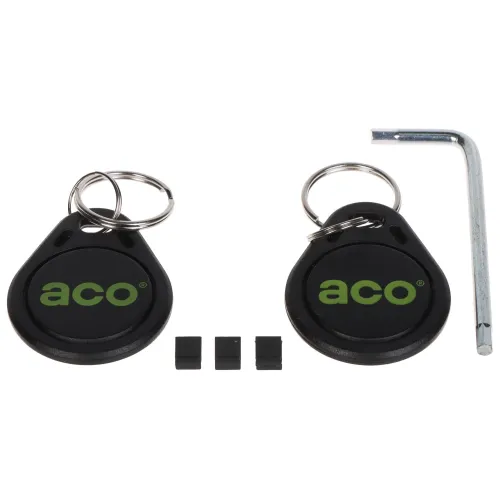 Na zdjęciu znajdują się dwa czarne breloki z logo "aco" oraz trzy małe czarne elementy. Obok nich leży metalowy klucz imbusowy.