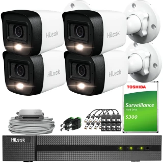 Zestaw do monitoringu składający się z czterech białych kamer HiLook, rejestratora, dysku twardego Toshiba oraz niezbędnych akcesoriów montażowych i kabli. Kamery mają kompaktowy, prostokątny kształt i są przeznaczone do montażu na ścianie.